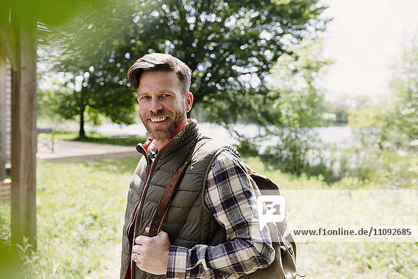 Portrait lächelnder Wanderer mit Rucksack im sonnigen Wald