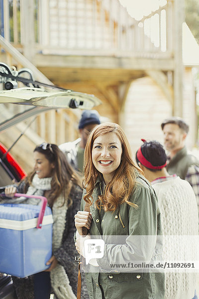 Portrait lächelnde Frau mit Freunden beim Entladen der Kühlbox vom Heck des Autos