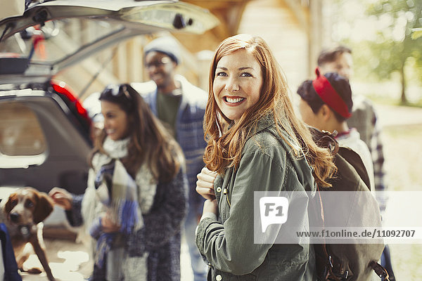 Portrait smiling hiker holding backpack with friends at back of car