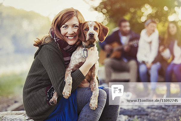 Portrait smiling woman hugging dog at campsite with friends