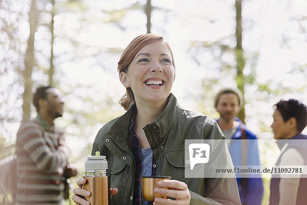 Smiling woman drinking coffee from insulated drink container hiking in woods