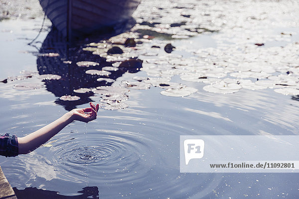 Wasser tropft aus der Hand der Frau am sonnigen See mit Seerosenblättern