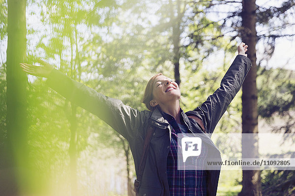 Exuberant woman hiking smiling with arms raised and head back in sunny woods