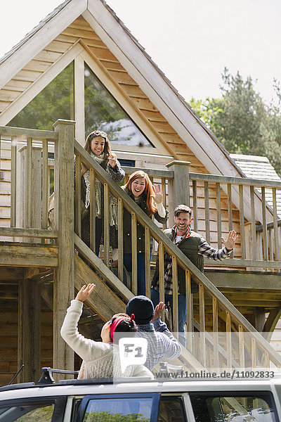 Friends on stairs waving to friends in car outside sunny cabin