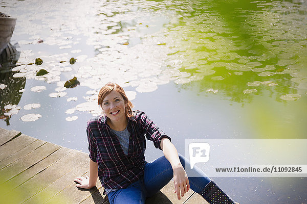 Portrait lächelnde Frau am sonnigen Ufer des Sees sitzend