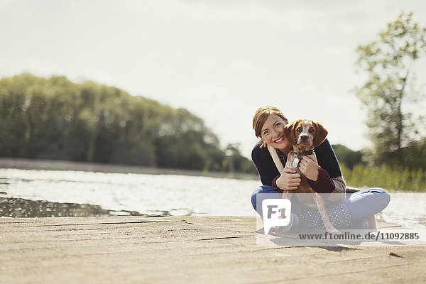 Portrait smiling woman hugging dog on sunny lakeside dock