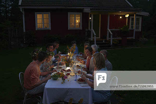 Familie genießt das Candle-Light-Dinner am Terrassentisch vor dem Haus bei Nacht.