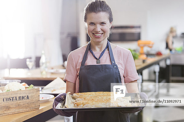 Portrait lächelnde Frau hält Tablett mit Lebensmitteln in der Küche des Kochkurses