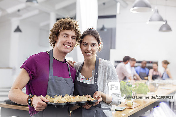 Portrait lächelndes Paar mit Tablett mit Essen in der Küche des Kochkurses