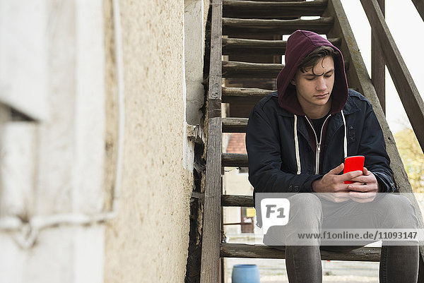 Young man text messaging on smart phone and sitting on wooden stairs