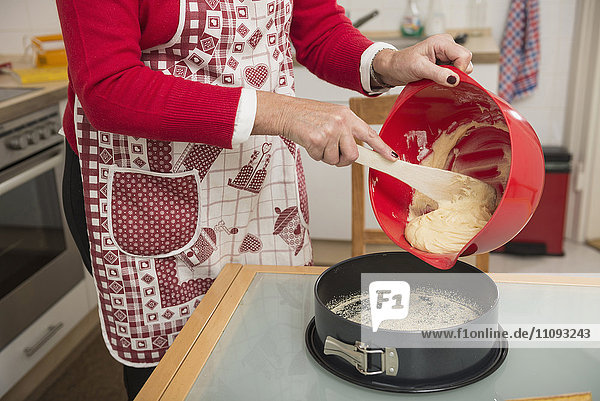 Senior woman pouring dough into a spring form pan