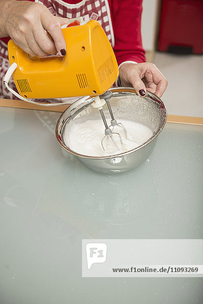 Senior woman mixing meringue in mixing bowl in kitchen