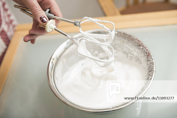Senior woman holding wire whisk over meringue filled bowl