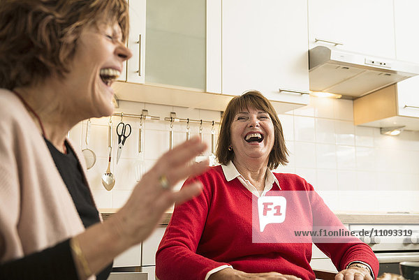Two senior women talking and laughing in kitchen