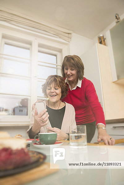 Two senior women using smart phone in kitchen