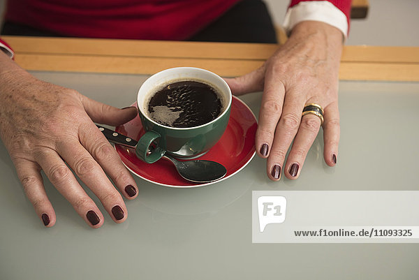 Nahaufnahme der Hand einer älteren Frau und schwarzer Kaffee auf dem Tisch