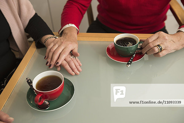 Hände zweier älterer Frauen trösten sich gegenseitig mit Kaffee auf dem Tisch