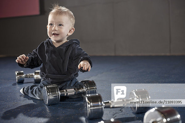 Nettes kleines Baby spielt mit Hanteln im Fitnessstudio