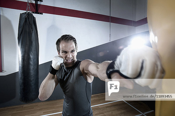 Sportler beim Krafttraining mit einem Boxsack im Fitnessstudio