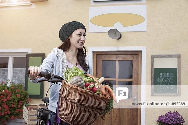 Mittlere erwachsene Frau mit Fahrrad und Gemüse vor einem Naturkostladen stehend
