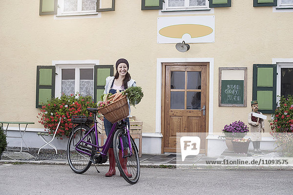 Porträt einer mittleren erwachsenen Frau mit Fahrrad und Gemüse auf der Straße vor einem Bioladen