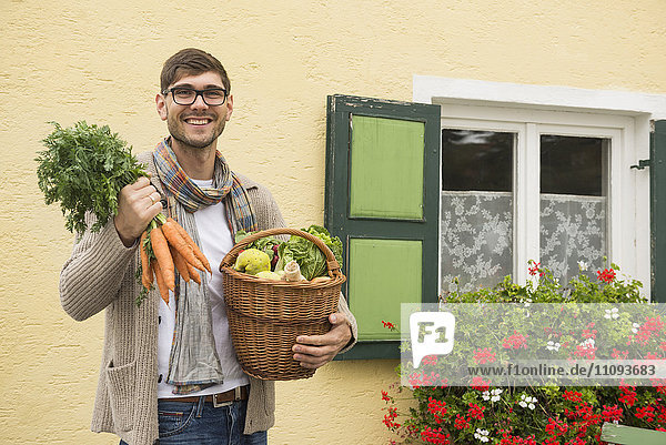 Porträt eines erwachsenen Mannes  der einen Korb voller Gemüse hält und lächelt
