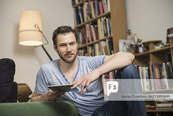 Mid adult man using digital tablet in living room  Munich  Bavaria  Germany