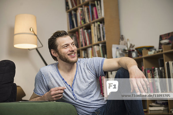 Mid adult man relaxing in living room and smiling  Munich  Bavaria  Germany