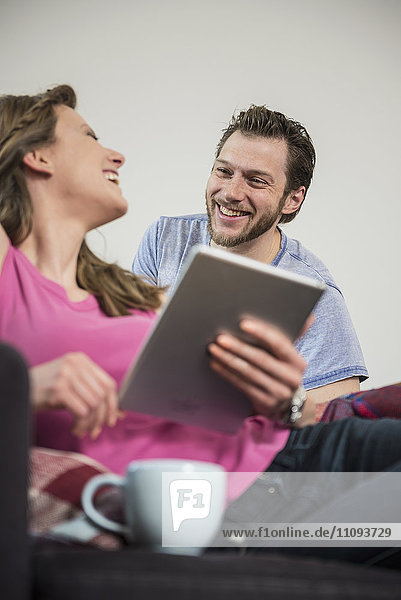 Couple using digital tablet in living room and smiling  Munich  Bavaria  Germany