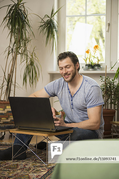 Mid adult man working on laptop in living room and smiling  Munich  Bavaria  Germany