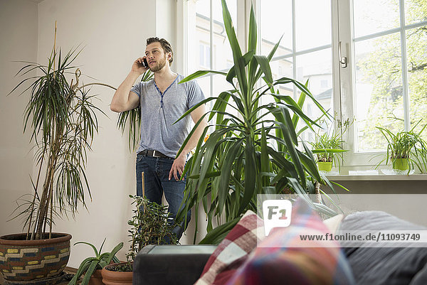 Mid adult man talking on mobile phone in living room  Munich  Bavaria  Germany