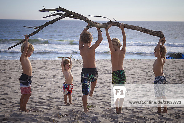 Eine Gruppe von Kindern hält einen Baumstamm am Strand hoch