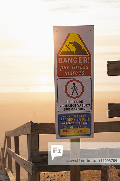 Gefahrenhinweisschild am Strand und Treppe hinunter zum Strand
