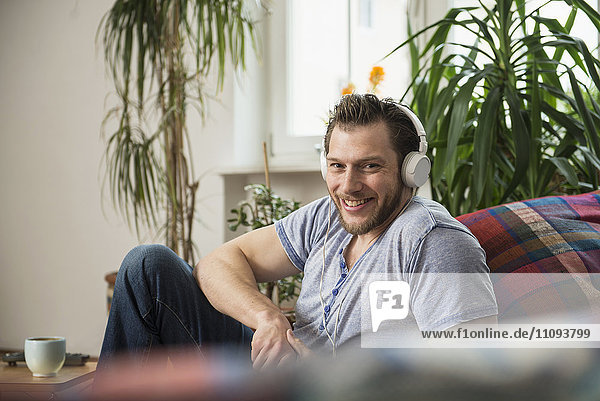 Mid adult man listening to music in living room and smiling  Munich  Bavaria  Germany