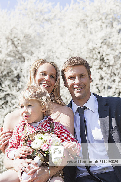 Newlywed couple with their son sitting in front of blossom tree