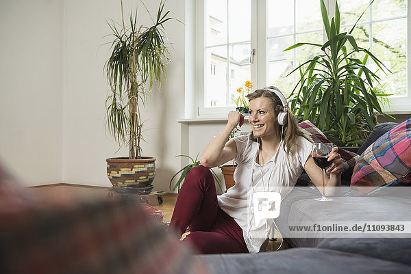 Young woman listening to music and drinking wine in living room  Munich  Bavaria