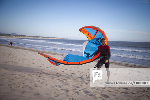 Junger Mann mit Kiteboard auf dem Strand