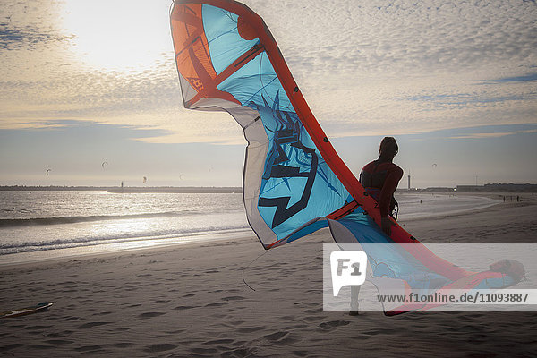 Junger Mann mit Kiteboard auf dem Strand