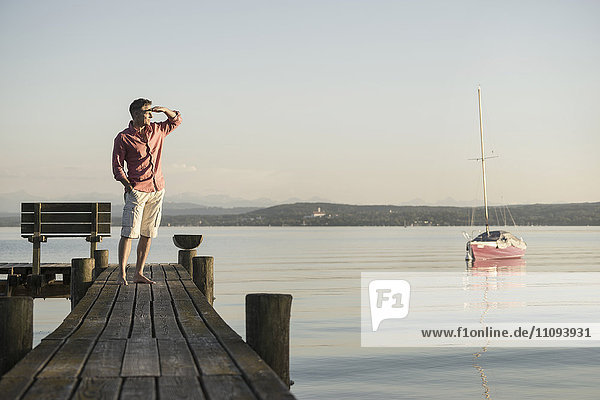 Mature man standing on wooden pier and looking at distance  Bavaria  Germany