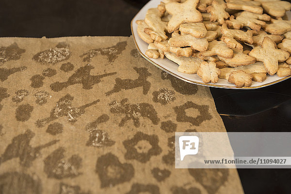 Verwendetes Backpapier mit unterschiedlich geformten Keksen im Teller