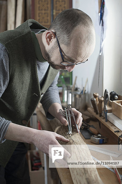 Männlicher Bogenbauer beim Anzeichnen auf Holz mit Zirkel in der Werkstatt  Bayern  Deutschland
