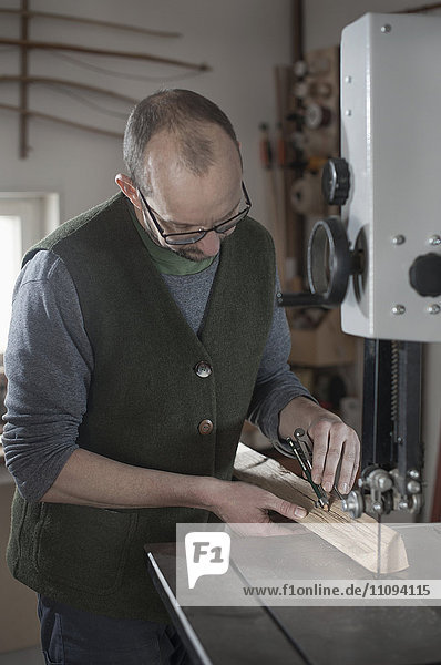 Männlicher Bogenbauer beim Anzeichnen auf Holz mit Zirkel in der Werkstatt  Bayern  Deutschland