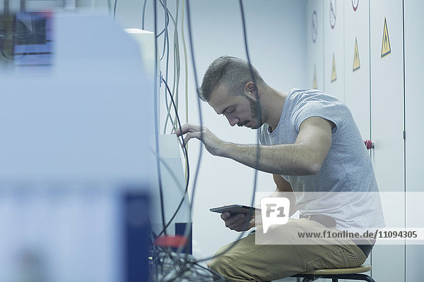 Männlicher Ingenieur  der ein digitales Tablet hält und ein Gerät im Labor repariert