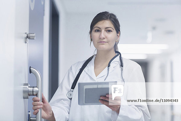Porträt einer jungen Ärztin  die in einem Krankenhauskorridor ein digitales Tablet benutzt