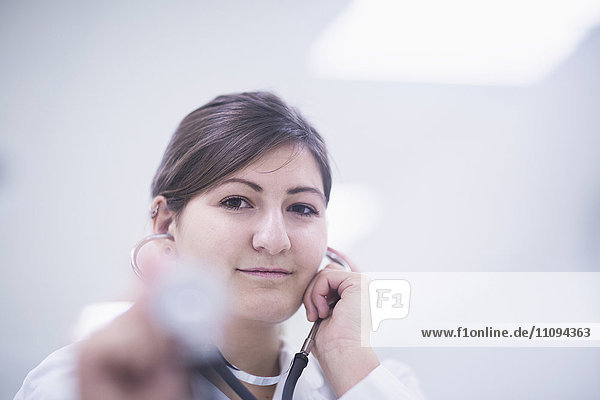 Porträt einer jungen Ärztin  die mit einem Stethoskop den Herzschlag abhört