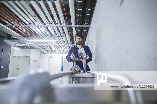 Junger männlicher Ingenieur mit Headset  der in einem Industriebetrieb eine Rohrleitungsverbindung überprüft