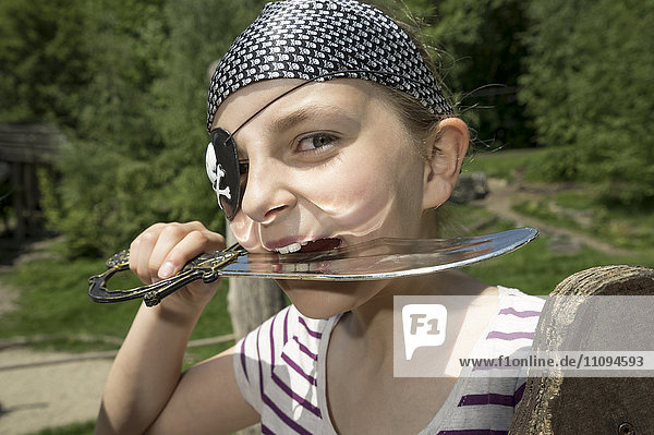 Portrait of a girl dressed up as a pirate biting saber in playground  Bavaria  Germany