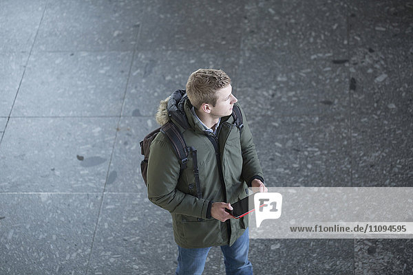 Blick von oben auf einen jungen Mann  der ein digitales Tablet hält und wegschaut