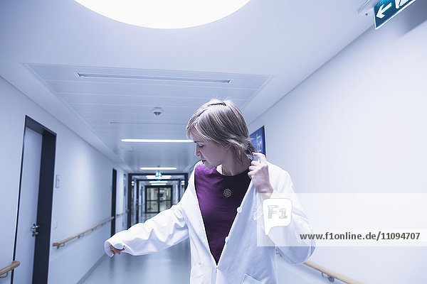 Junge Ärztin betrachtet ihre Hand beim Gehen im Krankenhausflur