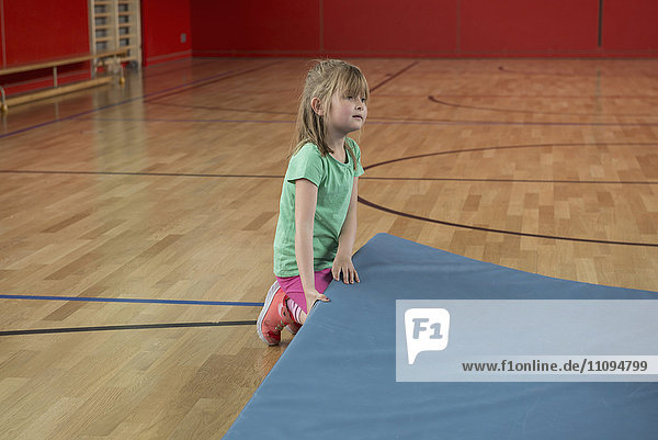 Mädchen versucht  eine schwere Übungsmatte im Basketballfeld einer Sporthalle hochzuheben  München  Bayern  Deutschland